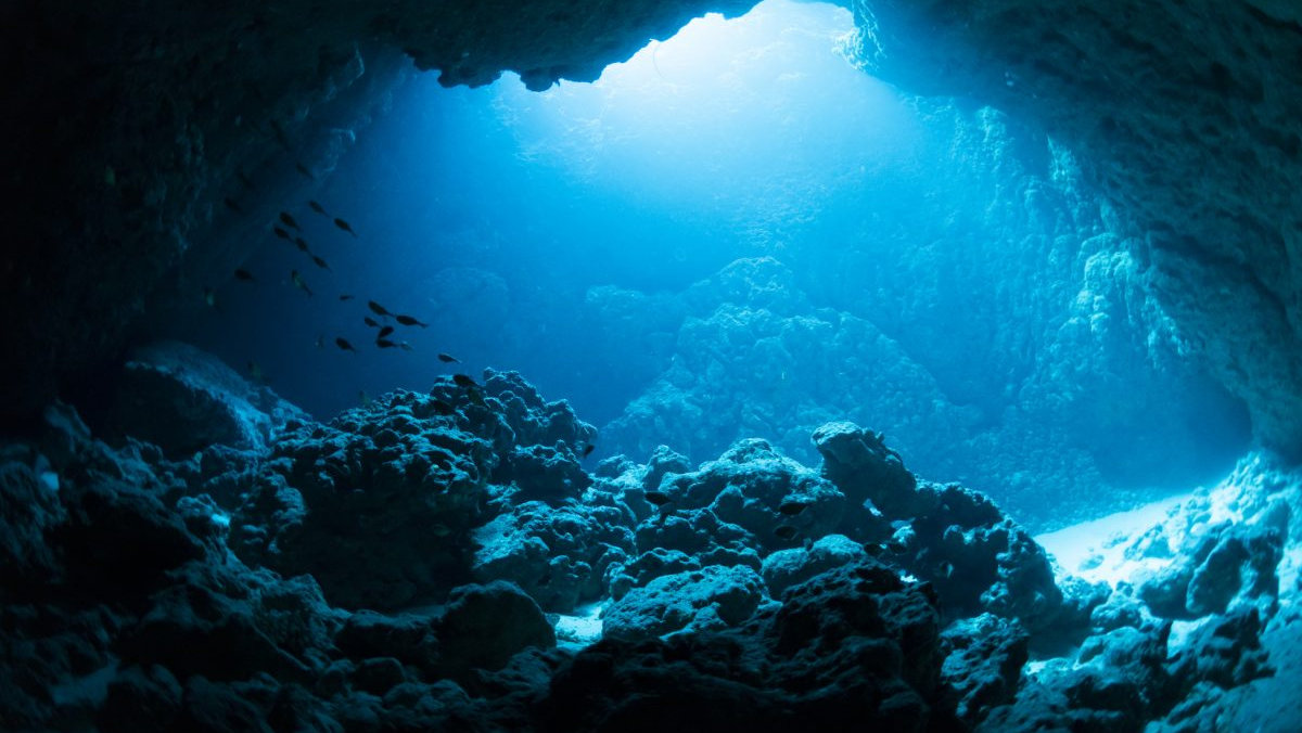 Underwater cave illuminated by blue light with rocky seabed formations.